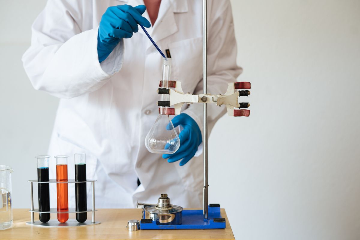 Laboratory technician in a white coat and blue gloves working with glassware and test tubes at a bench